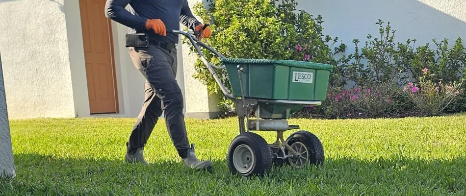 Man in New Smyrna Beach, FL, pushing a granular fertilizer spreader machine.
